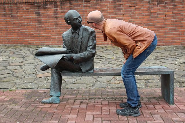 A man is standing next to a statue of a man reading.