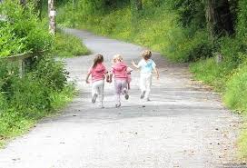 Three children running down a road with trees in the background.