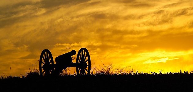 A cannon is sitting in the grass at sunset.