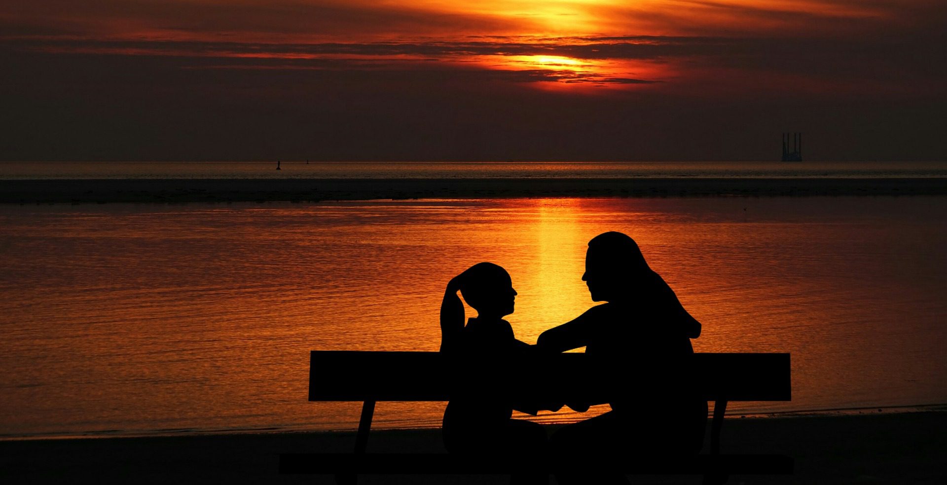 Two people sitting on a bench at sunset.